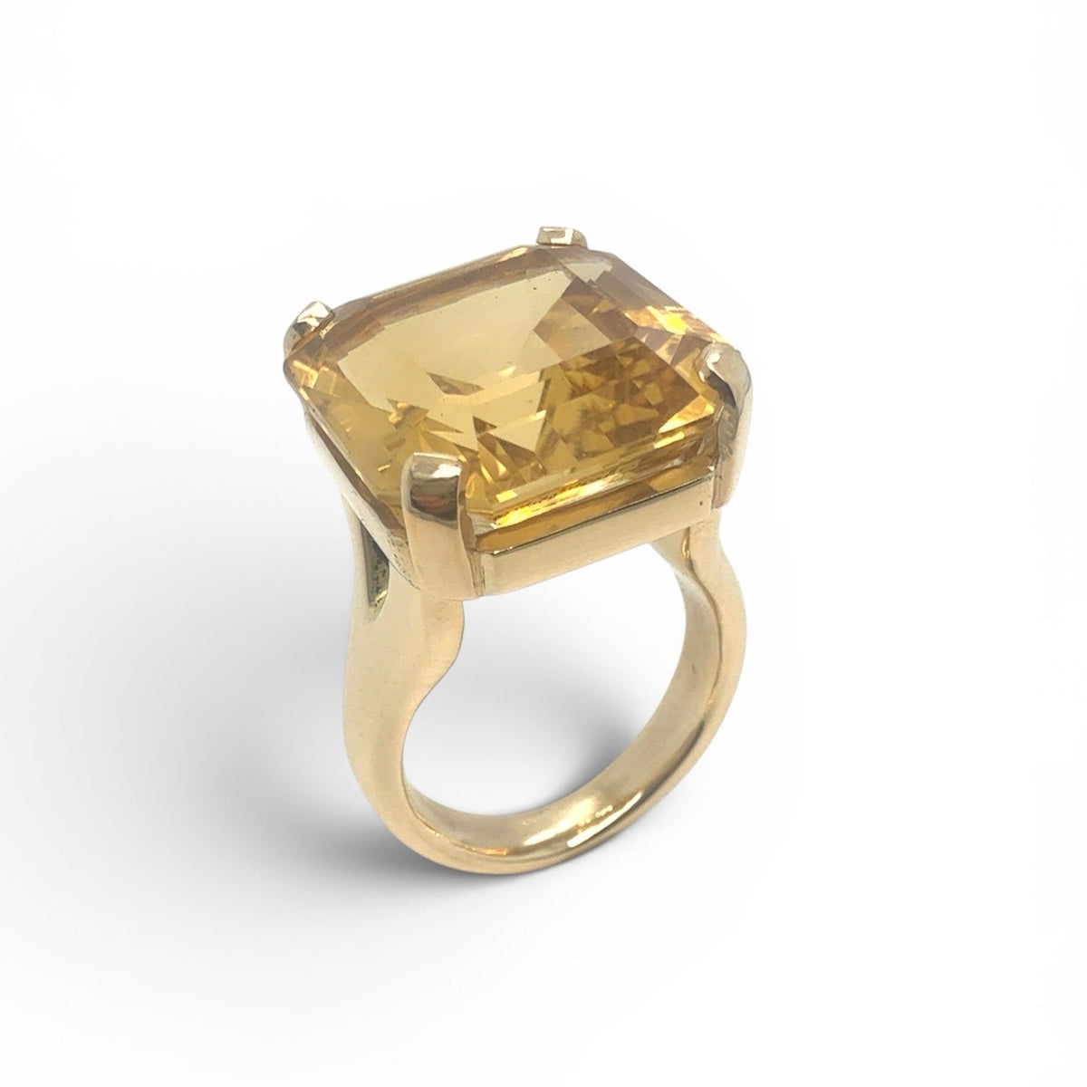 A gold ring featuring a large, cushion-cut yellow citrine gemstone in a four-prong setting, shown on a white background
